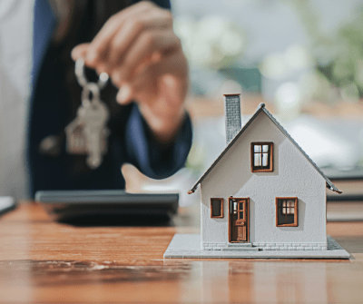 Maquette van een huisje, persoon erachter houdt sleutels vast